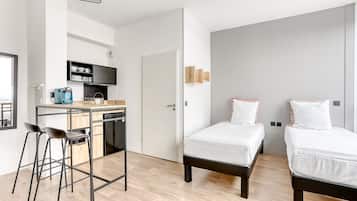 Quarto de hotel moderno com cozinha compacta, duas camas e um banquinho de bar.