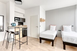 A modern hotel room with a kitchenette, two beds, and a bar stool. - Ecla Massy Palaiseau (Palaiseau)