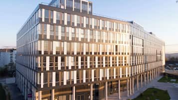 Um edifício moderno de vários andares com fachada de vidro, telhado plano e um pátio espaçoso.