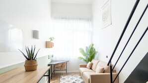 A modern living space with a wooden table, a beige sofa, a small table with a chair, and a potted plant. - Ecla Massy Palaiseau (Palaiseau)