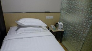 Habitación de hotel con cama, almohadas, mesita de noche con teléfono, botella de agua y cafetera.