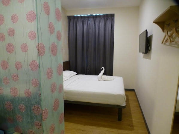 Una cama individual con un almohadón con forma de cisne, un televisor en la pared y una cortina con estampado floral.