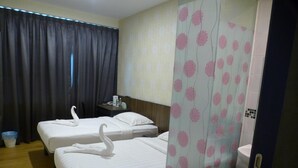 Habitación de hotel con dos camas, un escritorio pequeño, una silla, baño con inodoro y lavamanos, y cortina con estampado floral.