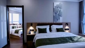 A modern hotel room with a large bed, bedside tables with lamps, a wall-mounted artwork, and a view through an open door. - Greentree Inn Tangshan Caofeidian District Nanbao Development Zone (Tangshan)