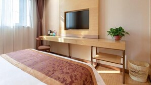 Ein Hotelzimmer mit Bett, Schreibtisch mit Flachbildfernseher, Topfpflanze und Korbwäsche.
