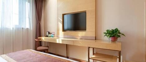 A hotel room with a bed, a desk with a flat-screen TV, a potted plant, and a wicker basket.