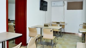 Ein Klassenzimmer mit Tischen und Stühlen, einer roten Tür, einem an der Wand montierten Fernseher und einer Klimaanlage.