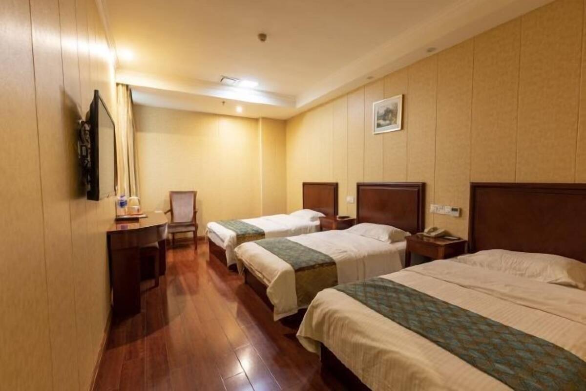 Traditional hotel room with two single beds and a large bed, a desk, and a telephone.