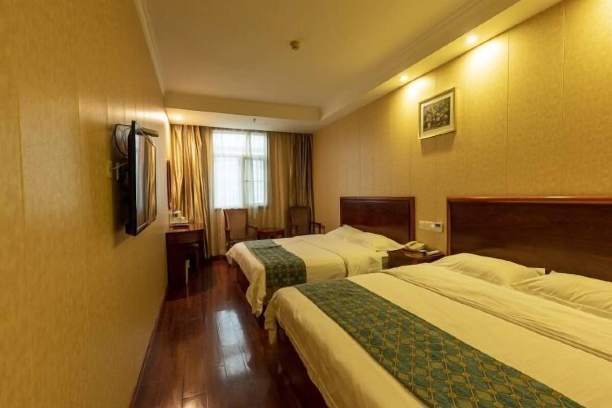 Two single beds with wooden headboards, a flat-screen TV, and a bedside table with a lamp.