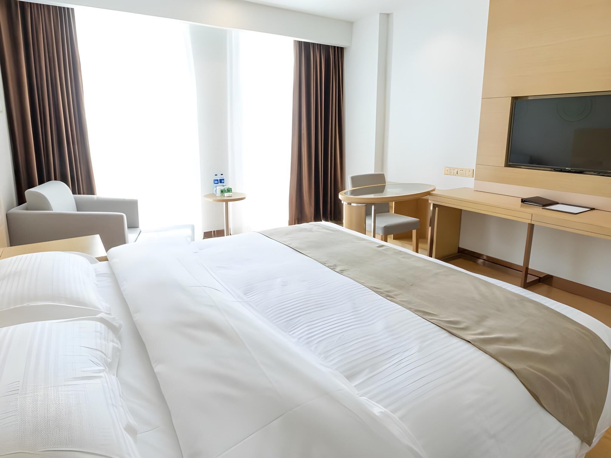 Une chambre d’hôtel avec un grand lit, un bureau, une chaise, une télévision et une fenêtre avec des rideaux.