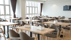 A modern dining area with multiple tables and chairs, large windows with curtains, and a flat-screen TV on the wall.