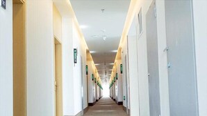 A long, narrow hotel corridor with doors on both sides, each marked with a green sign.