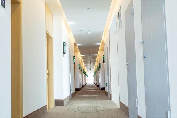 Ein langer, schmaler Hotelgang mit Türen an beiden Seiten, die jeweils mit einem grünen Schild gekennzeichnet sind.