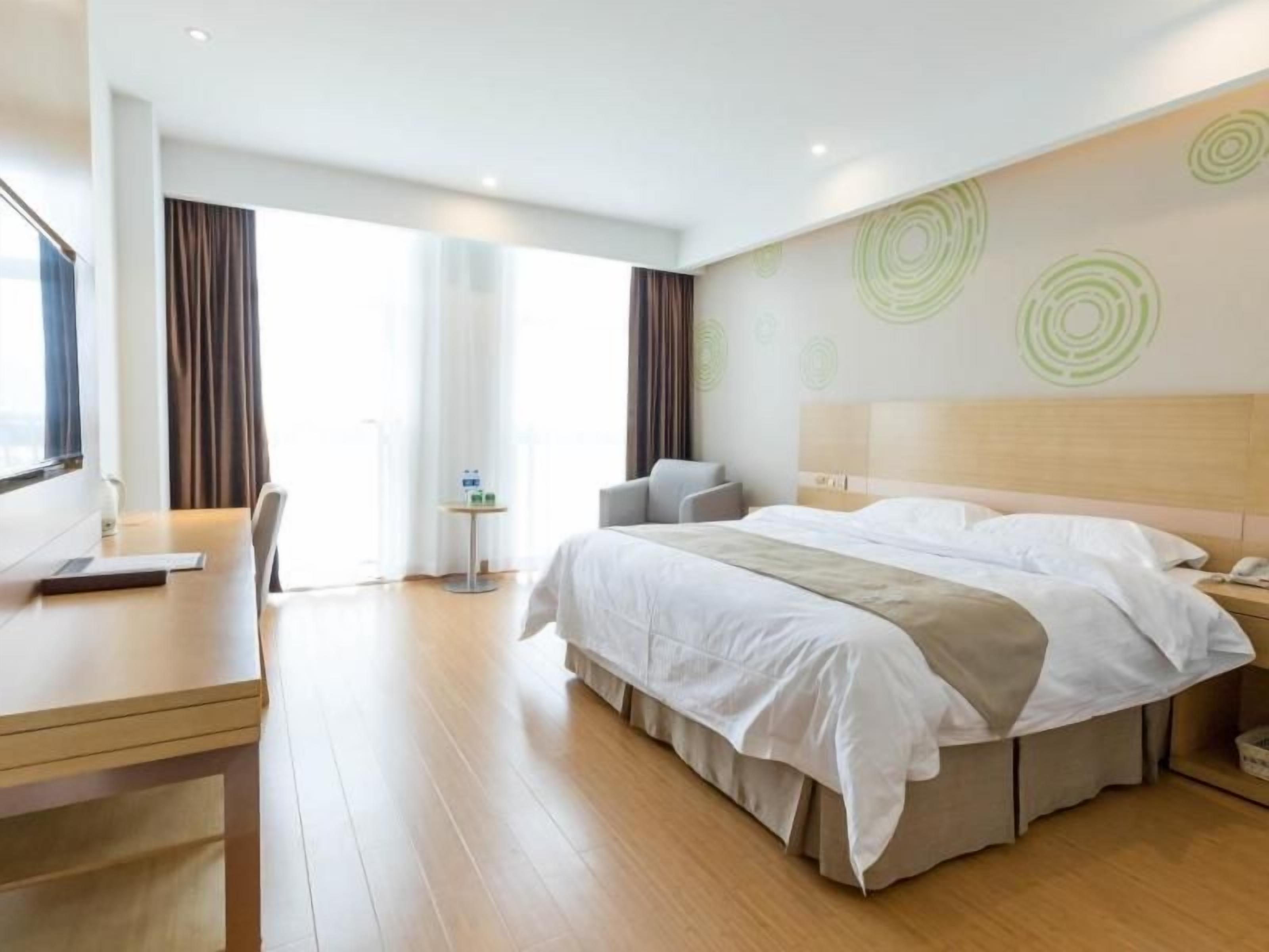 A modern hotel room with a large bed, a desk, and a view of the outdoors.