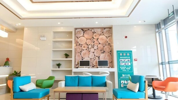 A modern lobby with a reception desk, seating area with sofas and chairs, a wall-mounted display, and a large window.