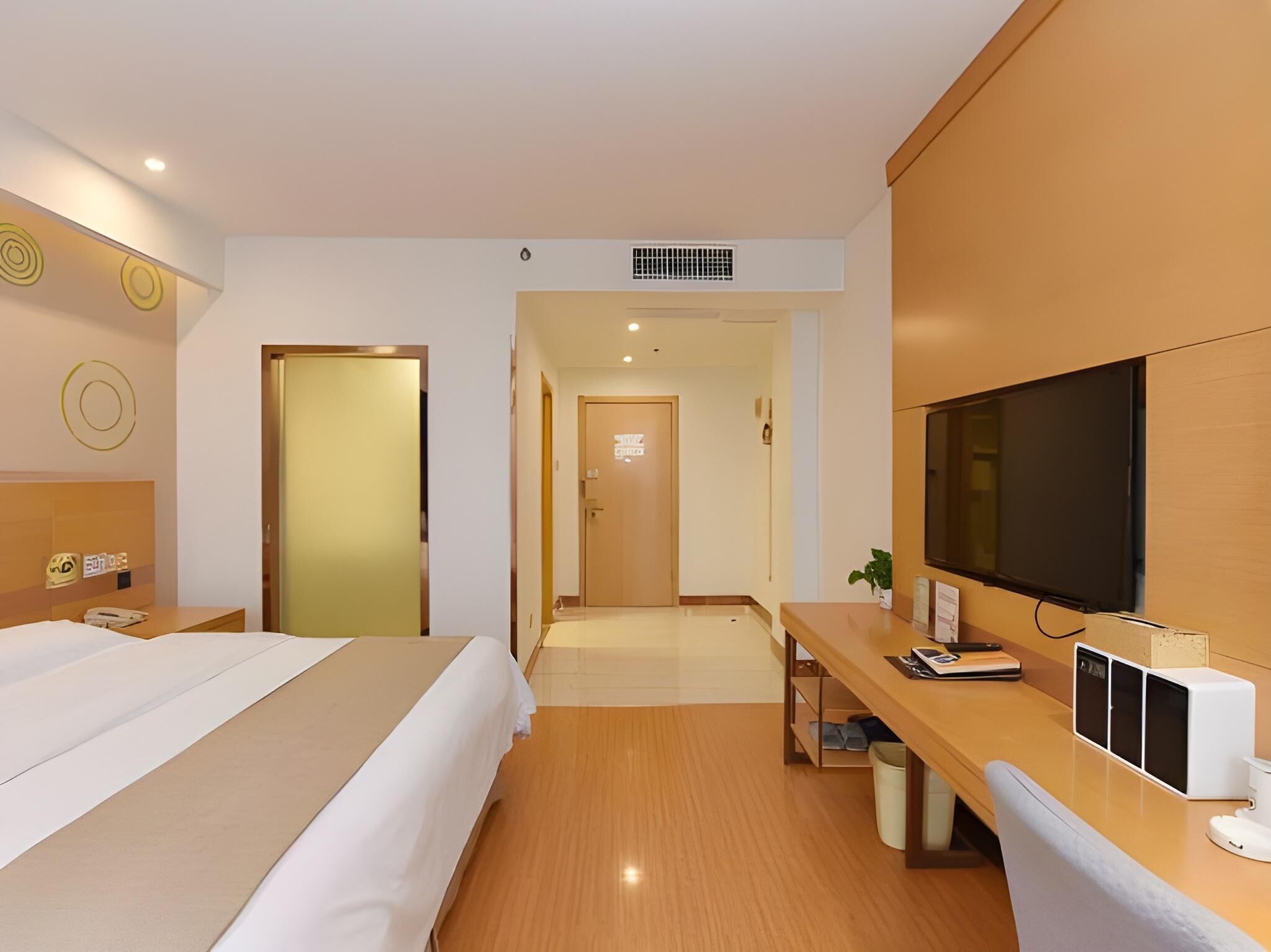 Een hotelkamer met een bed, een bureau met een computer, een televisie en een deur die naar een andere kamer leidt.