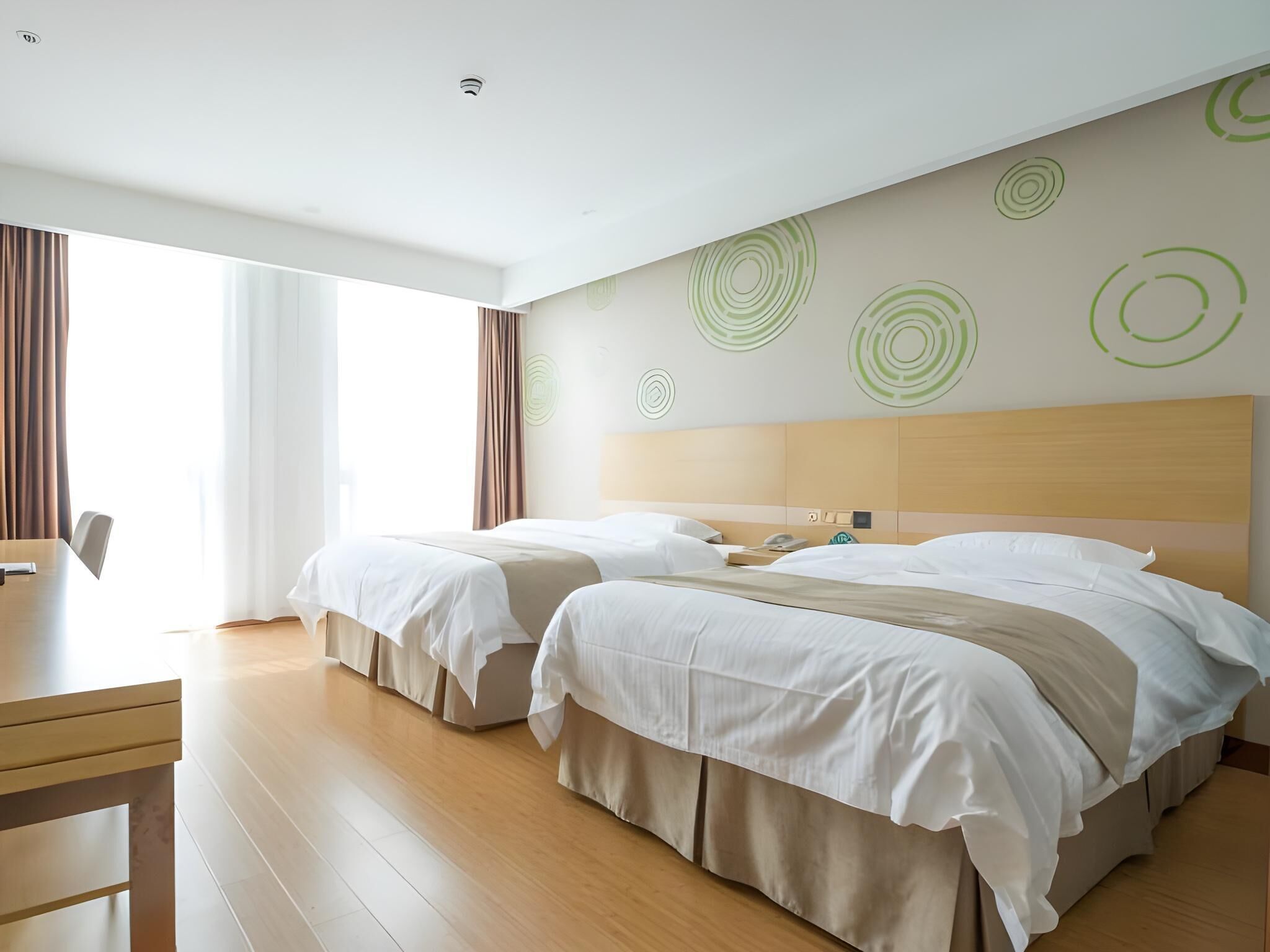Ein Hotelzimmer mit zwei Betten, einem Holztisch und einem großen Fenster mit Vorhängen.