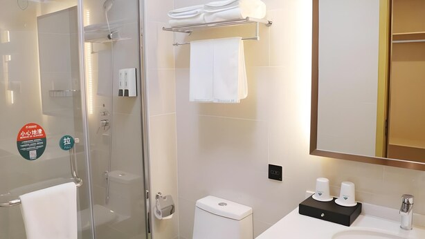 Une salle de bain moderne avec une douche à parois de verre, des toilettes, un lavabo avec un miroir et un porte-serviettes.