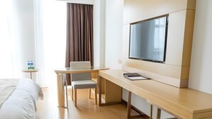 Une chambre d’hôtel comprenant un lit, un bureau avec une chaise, une télévision et une petite table avec des bouteilles d’eau.