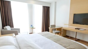 A hotel room with a large bed, a desk, a chair, a TV, and a window with curtains.