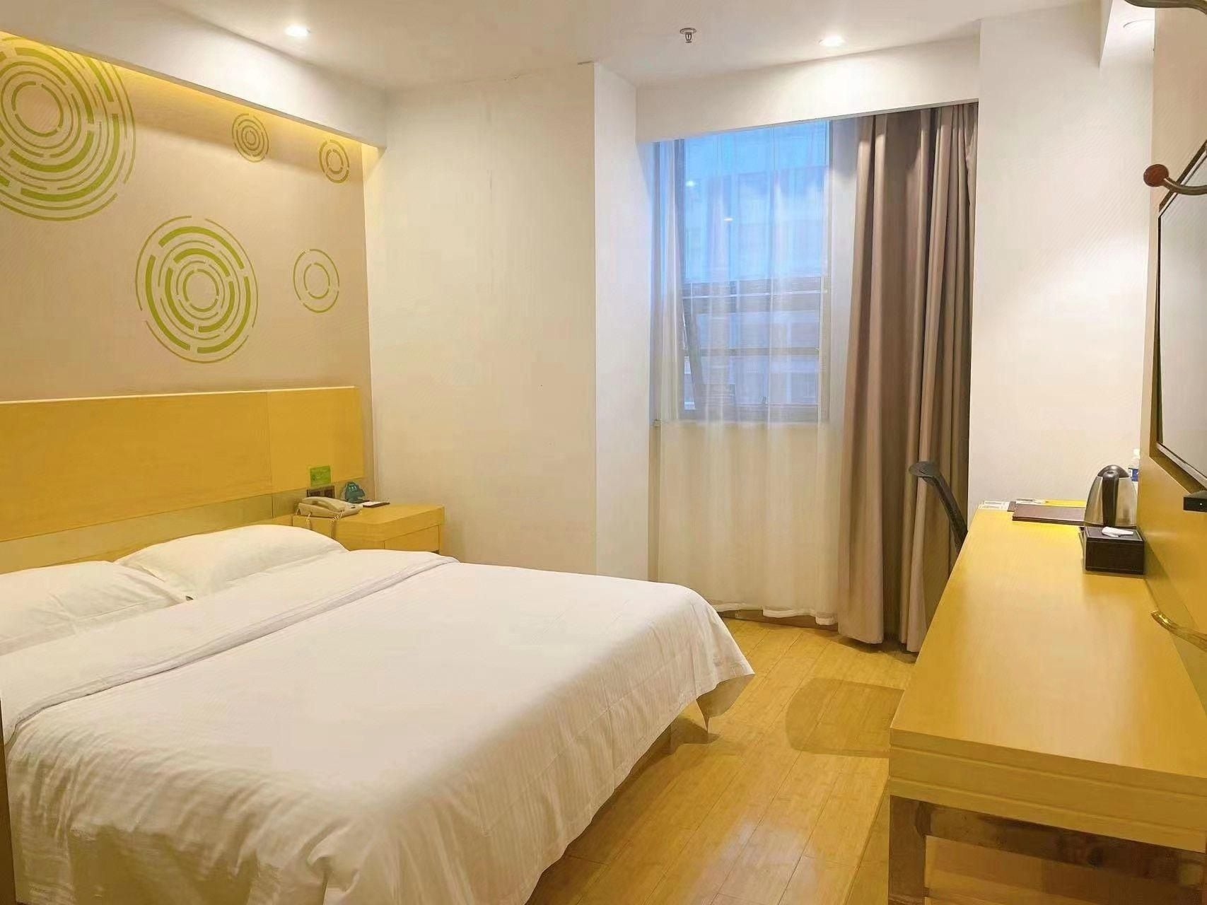 A hotel room with a bed, bedside table, lamp, and a window with curtains.