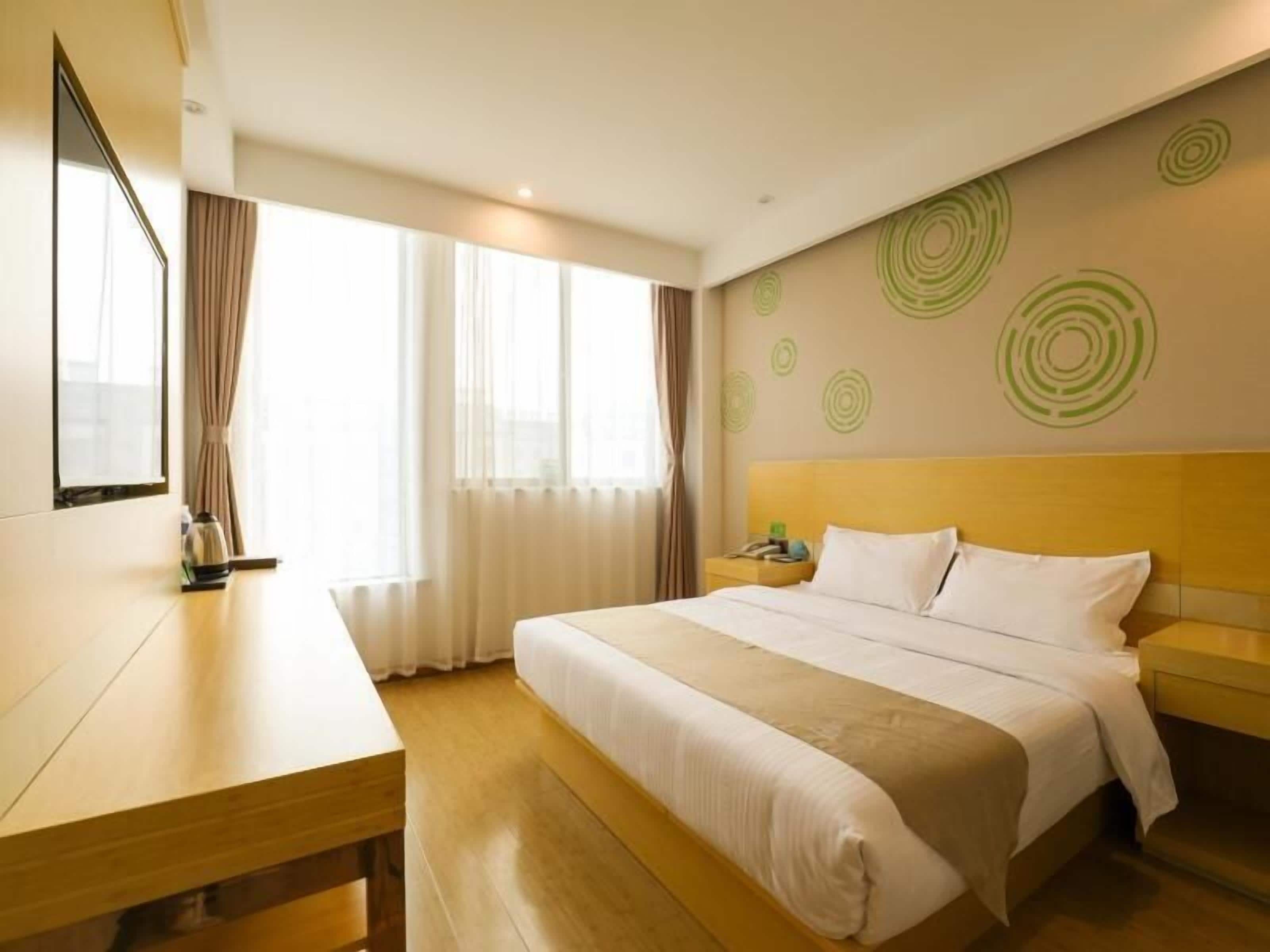 A hotel room with a bed, bedside table, and a large window with curtains.