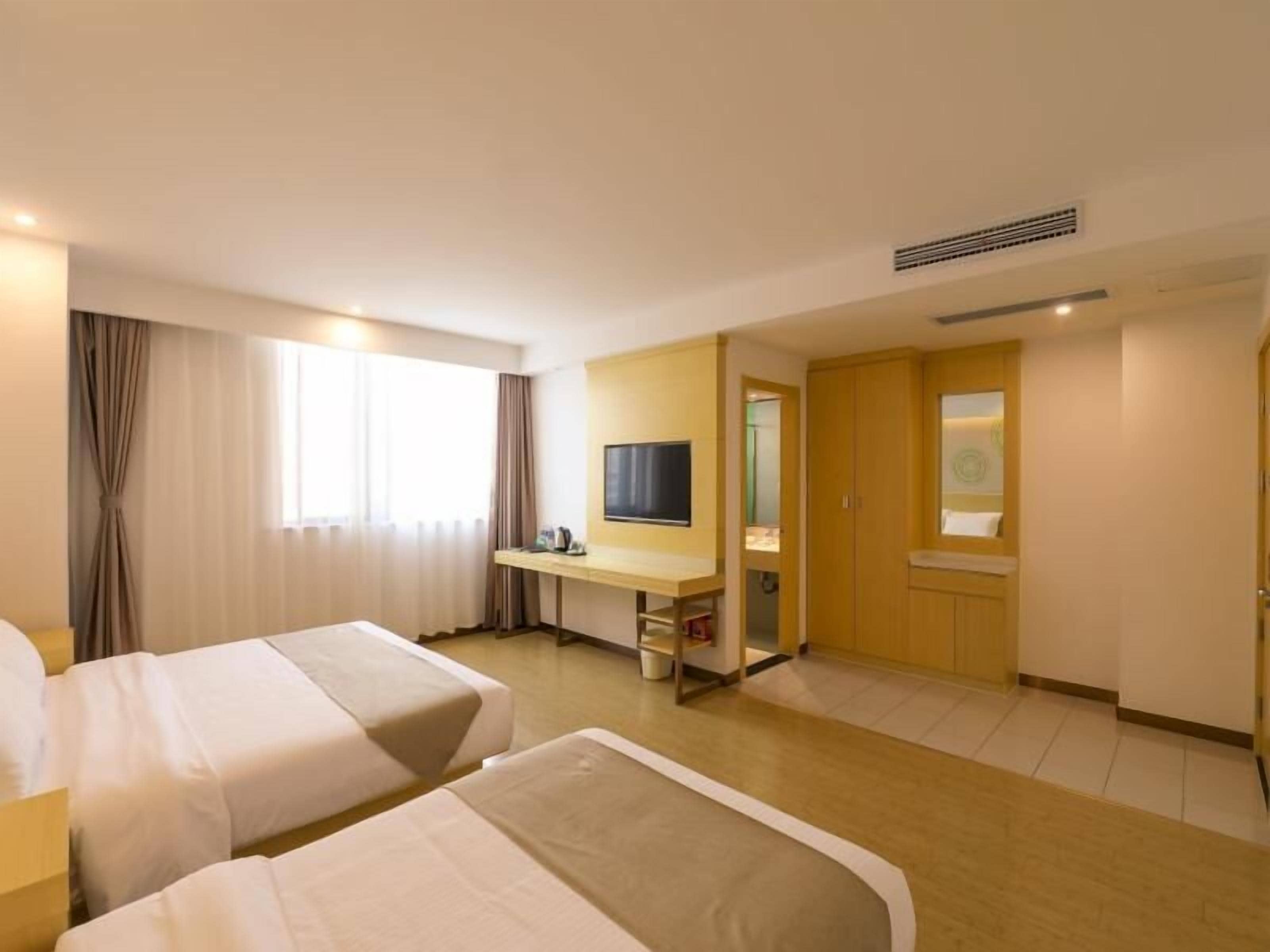 A hotel room with two beds, a desk with a TV, a mirror, and a wardrobe.