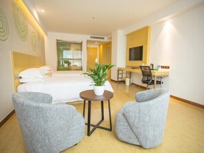 A hotel room with a bed, two grey armchairs, a small round table with a plant, a desk with a chair, and a TV on the wall. - Greentree Inn Wuxi Rongchuang Cultural Tourism City Nanquan Town Business Hotel (Wuxi)