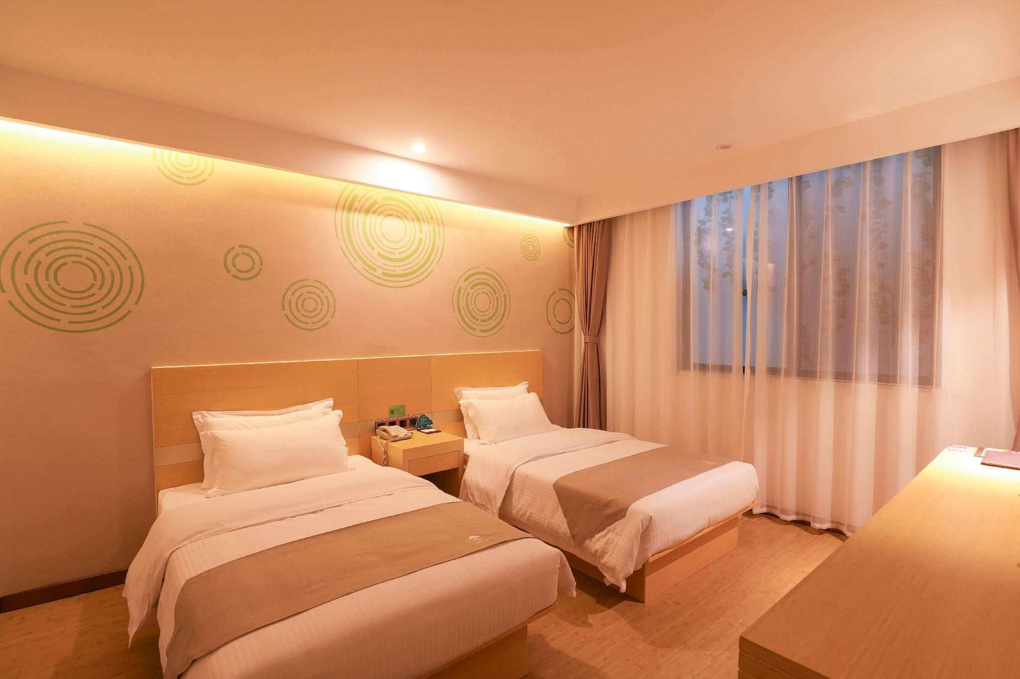 A hotel room with two beds, a bedside table with a phone, and a window with sheer curtains.