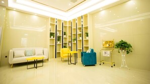 Eine moderne Lobby mit einem weißen Sofa, gelben Stühlen, einem türkisblauen Sessel und einer goldfarben gerahmten Dekoration.