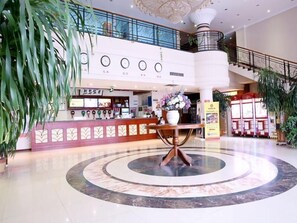 A hotel lobby with a reception desk, a circular marble floor, and a staircase leading to an upper level.