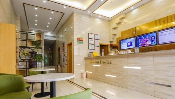 A reception area with a marble counter, green chairs, and a TV screen displaying information. - Greentree Inn Hefei Huainan Road Huaihe Garden (Hefei)