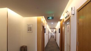 A hotel hallway with wooden doors, a carpeted floor, and a green exit sign. - Greentree Inn Hefei Huainan Road Huaihe Garden (Hefei)