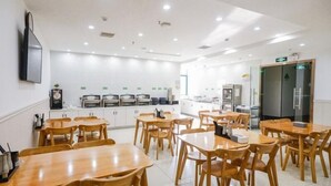 A spacious dining area with wooden tables and chairs, a kitchen in the background, and a flat-screen TV mounted on the wall. - Greentree Inn Hefei Huainan Road Huaihe Garden (Hefei)