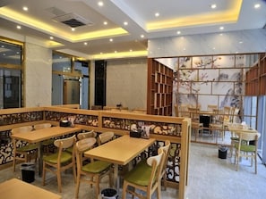 Interior de restaurante con mesas y sillas de madera, una pared decorativa con obras de arte y un diseño de techo moderno.