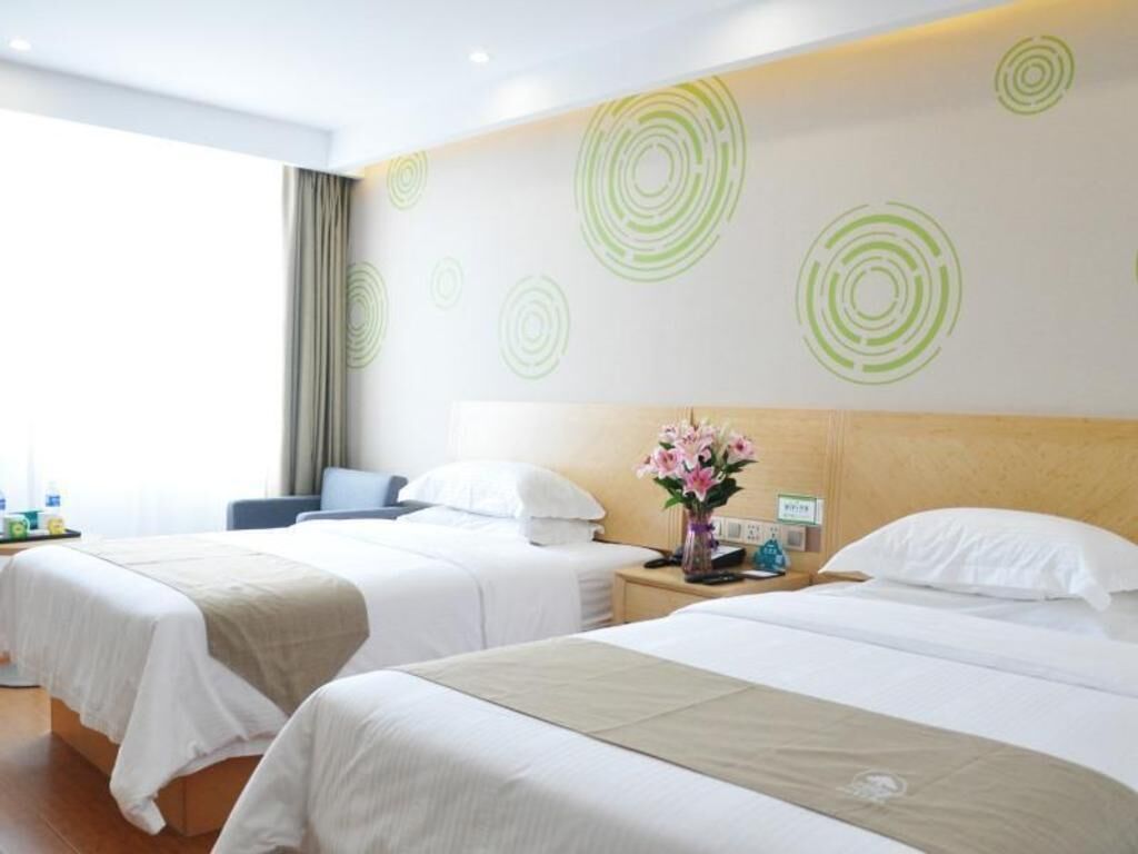 A hotel room with two beds, a nightstand with a vase of flowers, and a wall with circular patterns.