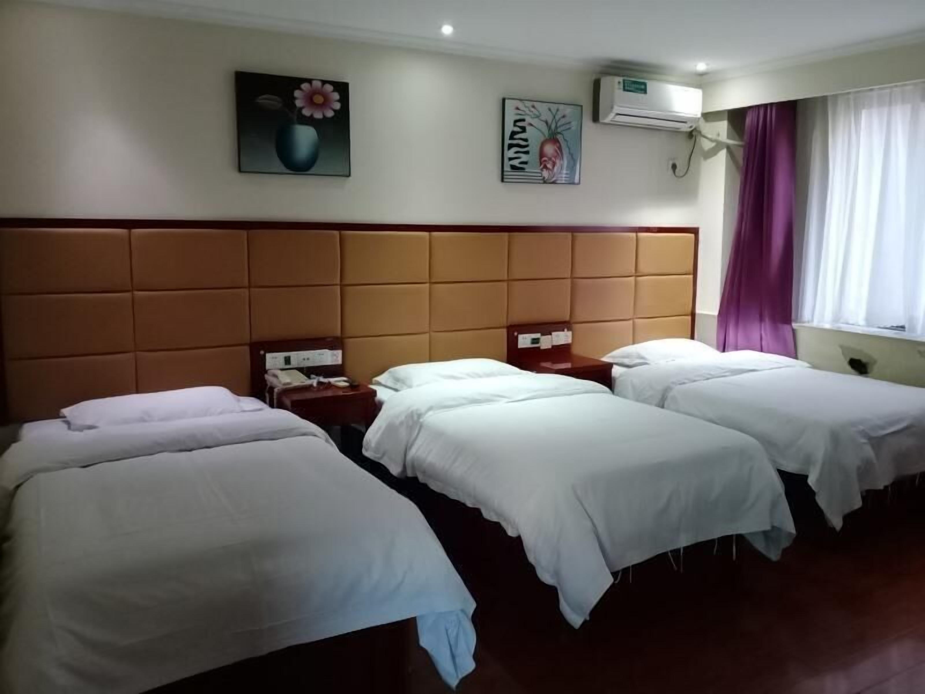 A hotel room with three single beds, a padded headboard, a bedside table with a phone, and a wall-mounted air conditioner.