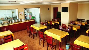A dining area with multiple tables and chairs, a kitchen area with appliances and utensils, and a red door. - Greentree Inn Shandong Dezhou Qihe County Party Committee Qilu Street Express Hotel (Dezhou)