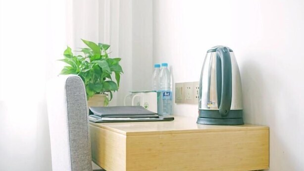 A small wooden desk with a laptop, a kettle, a water bottle, and a potted plant. - Greentree Inn Gongqingcheng City Golf Avenue Peopl (Jiujiang)