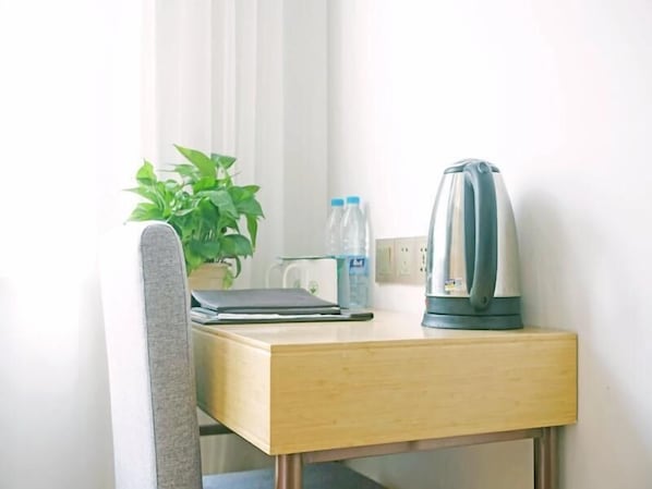 A small wooden desk with a laptop, a kettle, a water bottle, and a potted plant. - Greentree Inn Gongqingcheng City Golf Avenue Peopl (Jiujiang)