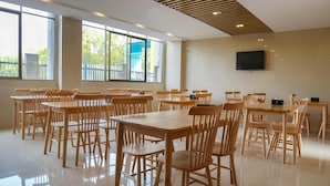 A spacious dining area with multiple wooden tables and chairs, large windows with a view of greenery, and a flat-screen TV mounted on the wall. - Greentree Inn Gongqingcheng City Golf Avenue Peopl (Jiujiang)