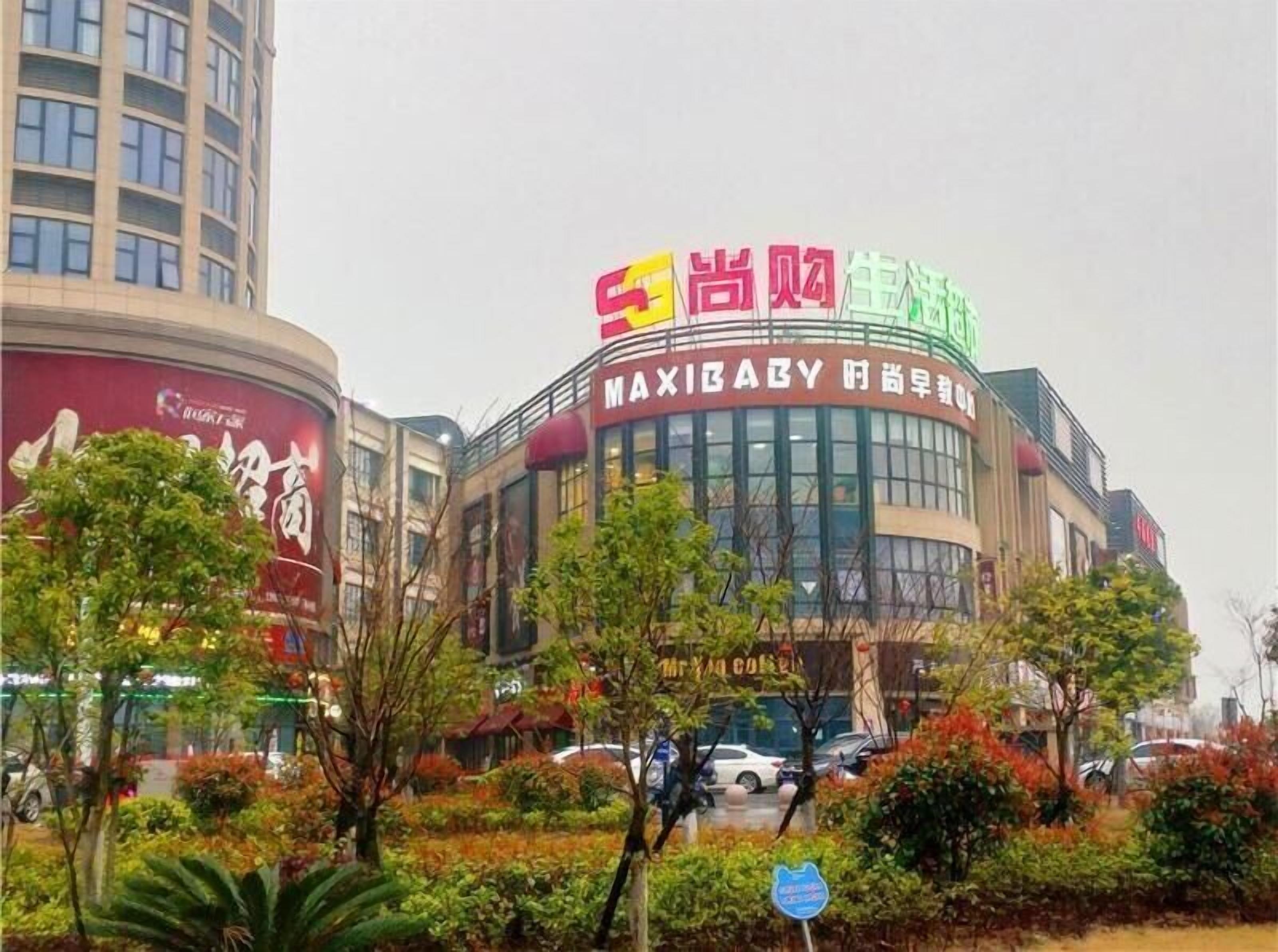 A commercial building with a large sign in multiple languages, surrounded by trees and parked cars.