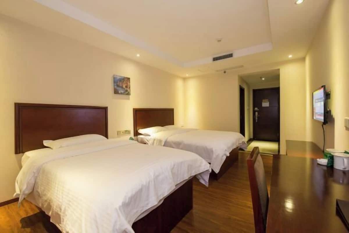 A hotel room with two beds, wooden headboards, a wooden table, and a television.