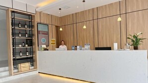 A reception desk with a white counter, wooden panel walls, hanging pendant lights, a wine rack, and a potted plant. - GreenTree Inn Jiangxi Shangrao Wuyuan Bus Station Tang Village Express Hotel (Wuyuan)
