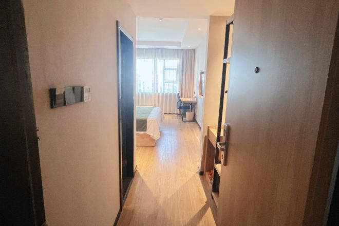 A hotel corridor with a bed, a desk, and a chair in the background.