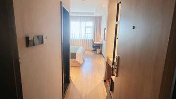 A hotel corridor with a bed, a desk, and a chair in the background.