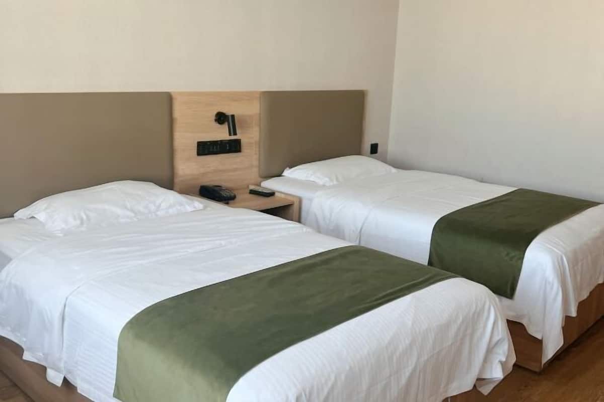 A hotel room with two beds, a wooden headboard, a nightstand, and a wall-mounted control panel.