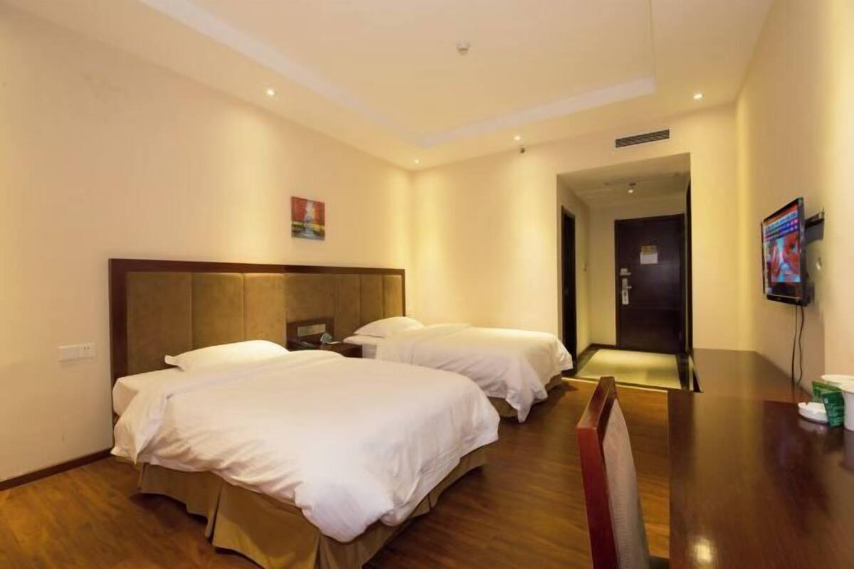 A hotel room with two beds, a wooden floor, a TV on the wall, and a door leading to another room.