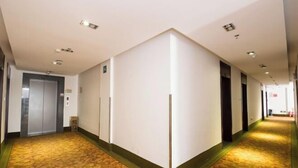 A hotel corridor with a patterned carpet, a central elevator, and a hallway leading to a door. - GreenTree Inn Jiangxi Shangrao Wuyuan Bus Station Tang Village Express Hotel (Wuyuan)