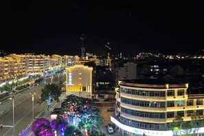 Un edificio de varios pisos con fachada curva, un patio central y una calle con árboles iluminados.